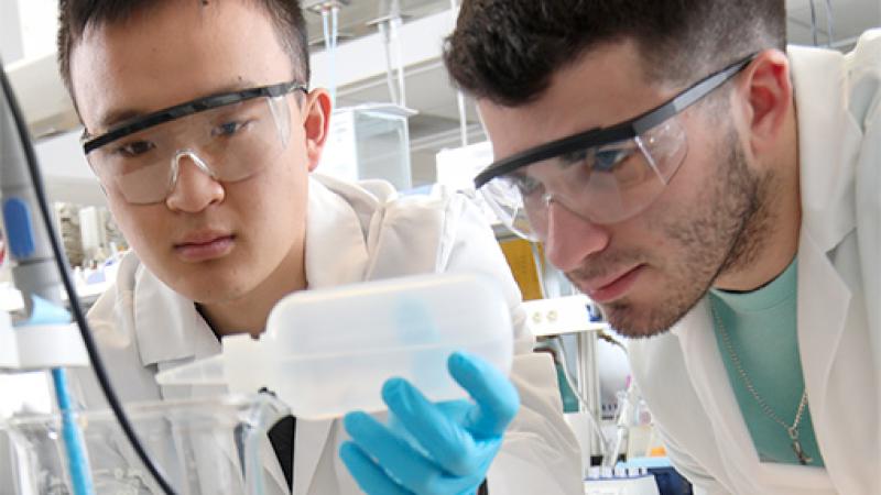 Two male researchers adding chemicals to research in a lab